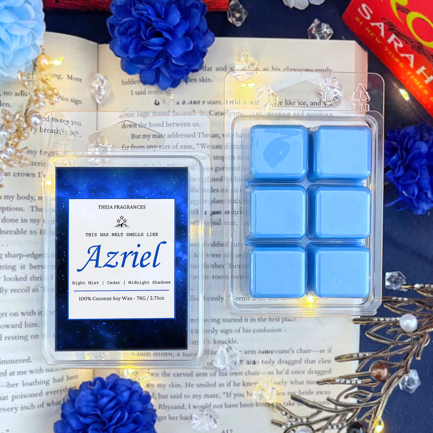 The 'Spymaster' coconut soy wax candle by Theia Fragrances is demonstrated in the 78G rectangular wax melt. The label features a blue galaxy. It is styled on an open book with decorative crystals and flowers.