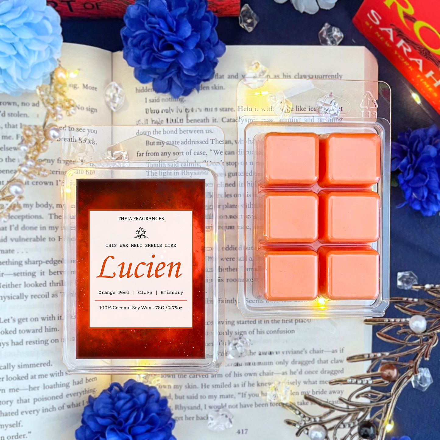 The 'Emissary' coconut soy wax candle by Theia Fragrances is demonstrated in the 78G wax melt. The label features an orange galaxy. It is styled on an open book with decorative crystals and flowers.