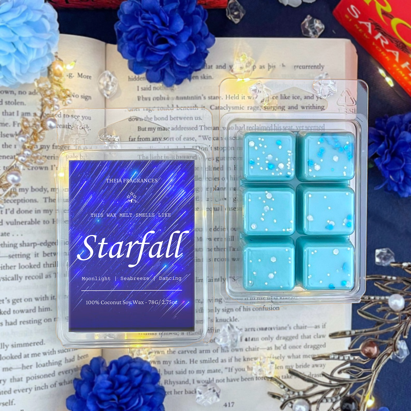 The 'Starfall' coconut soy wax candle by Theia Fragrances is demonstrated in the 78G rectangular wax melt. The label features a blue starry sky. It is styled on an open book with decorative crystals and flowers.