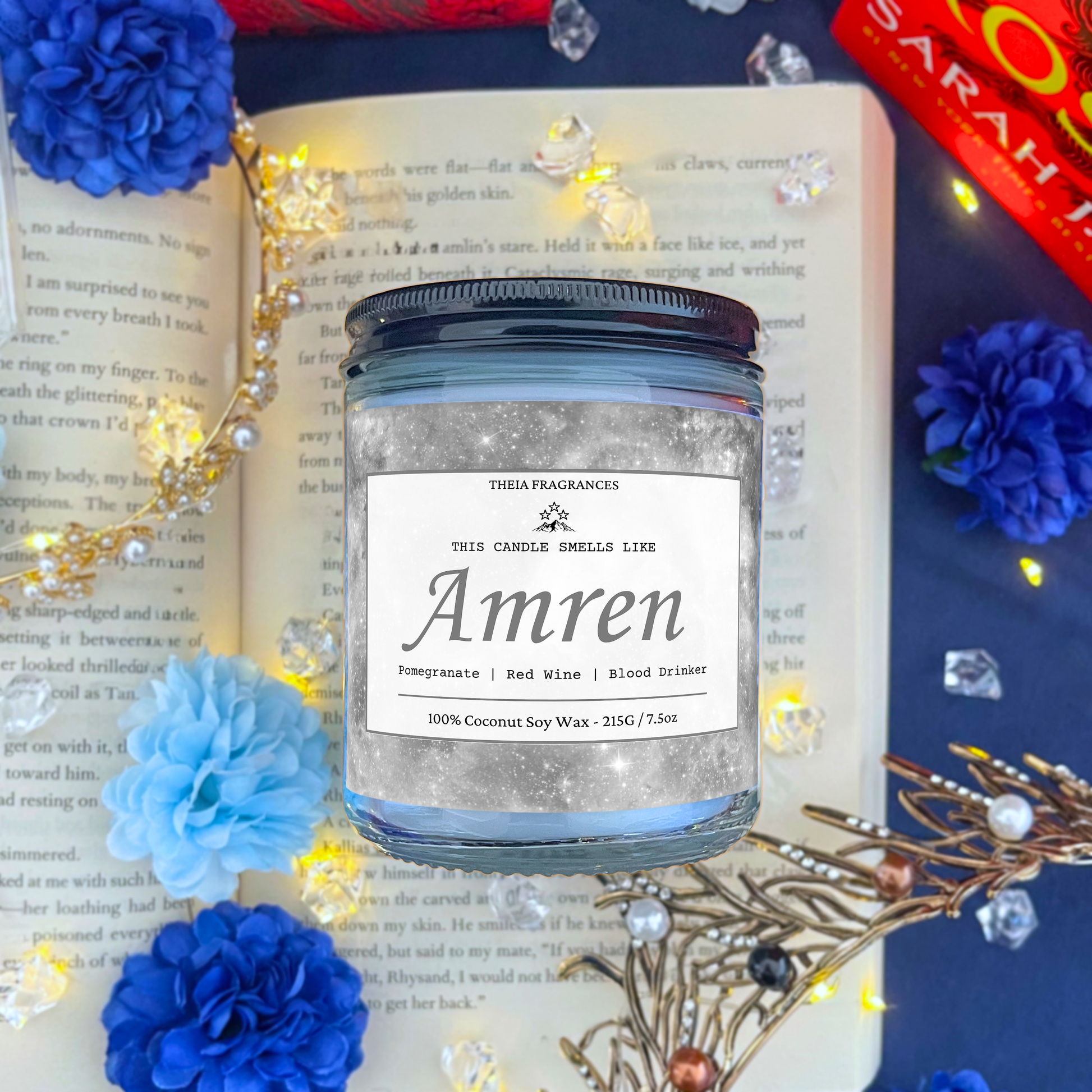 The 'Tiny Ancient One' coconut soy wax candle by Theia Fragrances is demonstrated in the 215G glass jar with a black lid. The label features a grey galaxy. It is styled on an open book with decorative crystals and flowers.