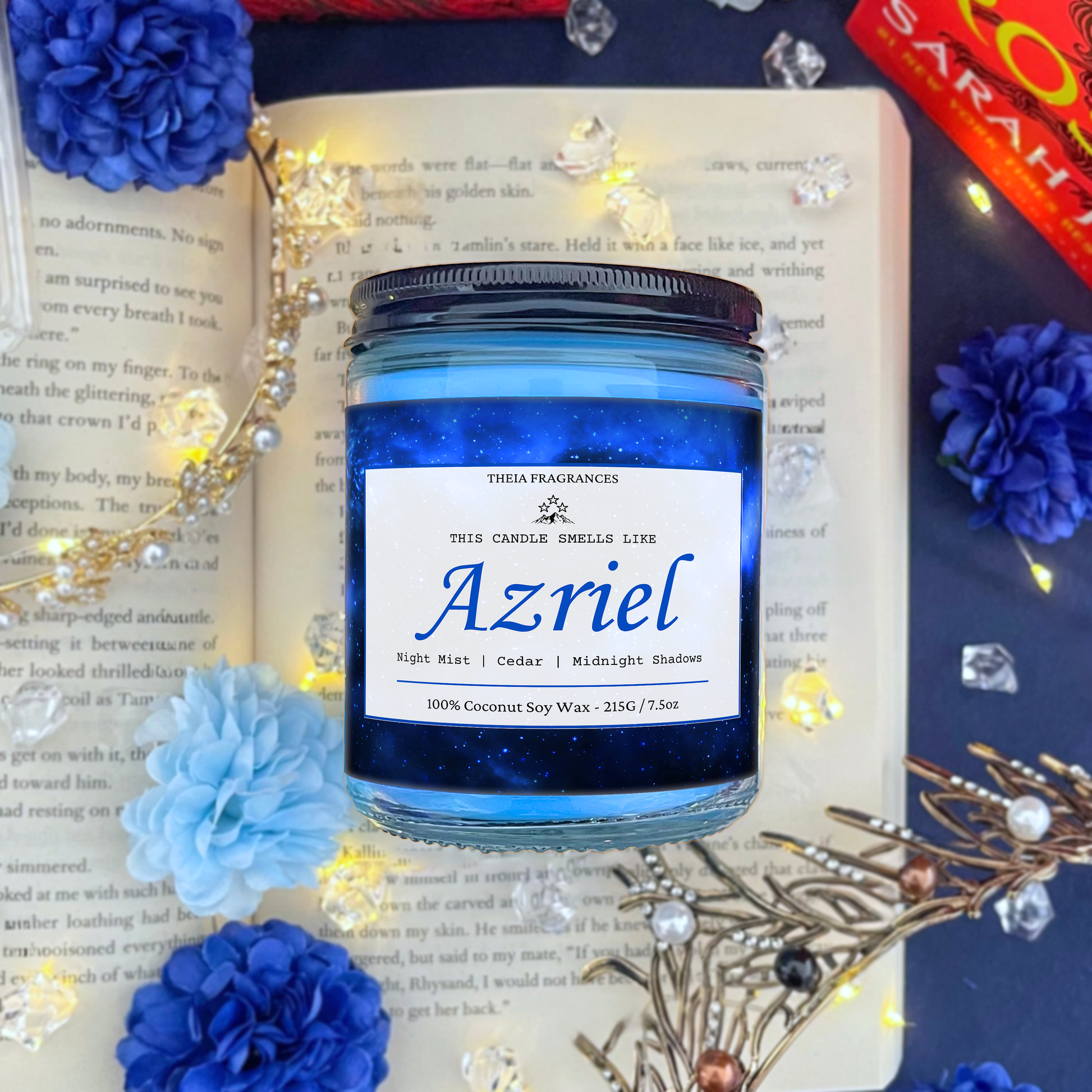 The 'Spymaster' coconut soy wax candle by Theia Fragrances is demonstrated in the 215G glass jar with a black lid. The label features a blue galaxy. It is styled on an open book with decorative crystals and flowers.