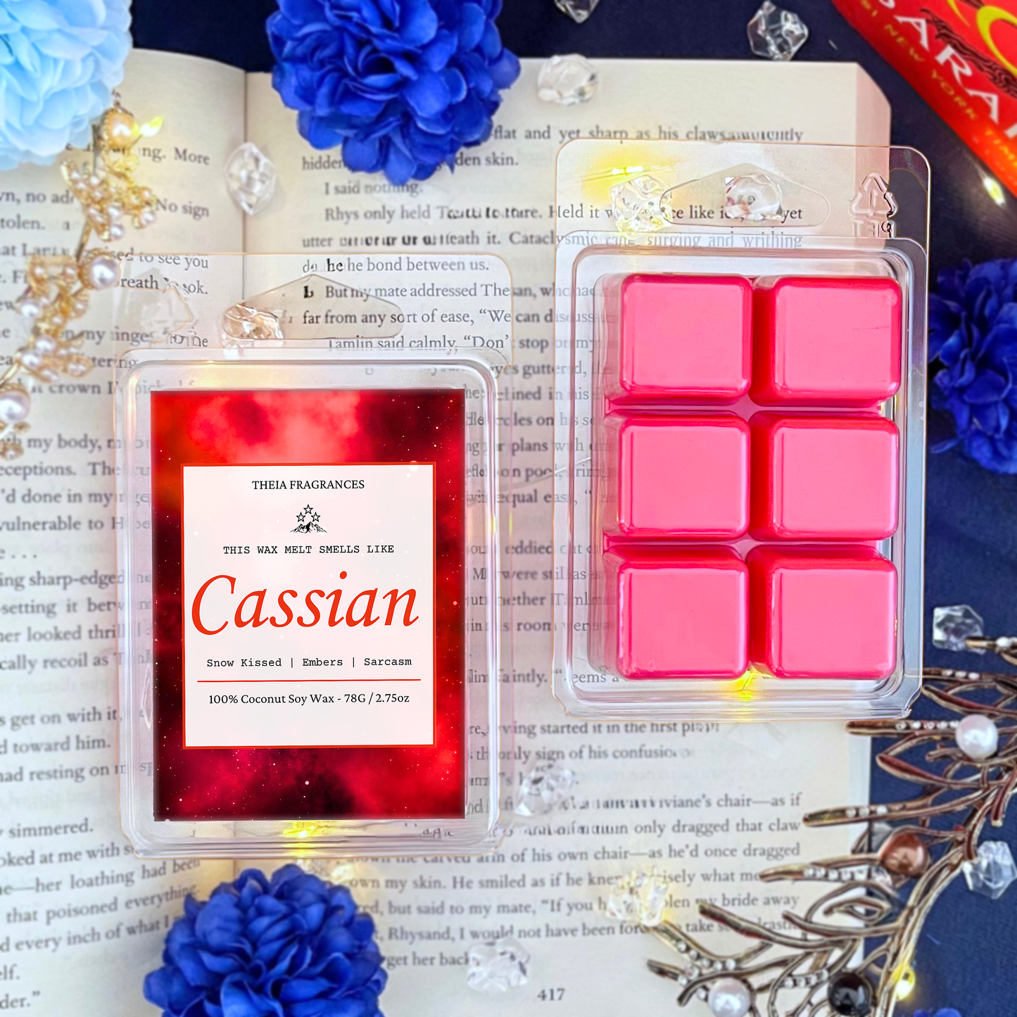 The 'Sarcastic Illyrian Warrior' coconut soy wax candle by Theia Fragrances is demonstrated in the 78G rectangular wax melt. The label features a red galaxy. It is styled on an open book with decorative crystals and flowers.