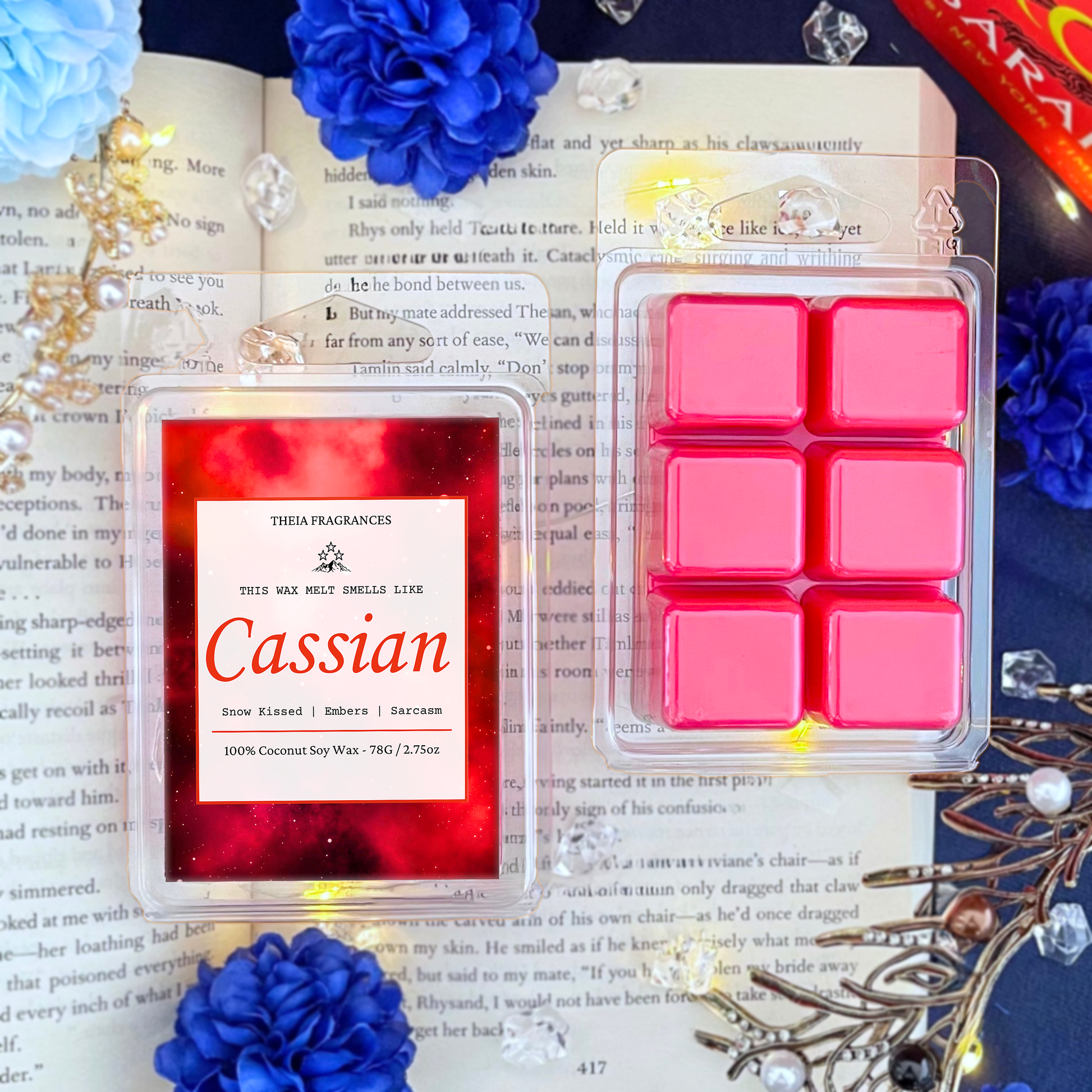 The 'Sarcastic Illyrian Warrior' coconut soy wax candle by Theia Fragrances is demonstrated in the 78G rectangular wax melt. The label features a red galaxy. It is styled on an open book with decorative crystals and flowers.
