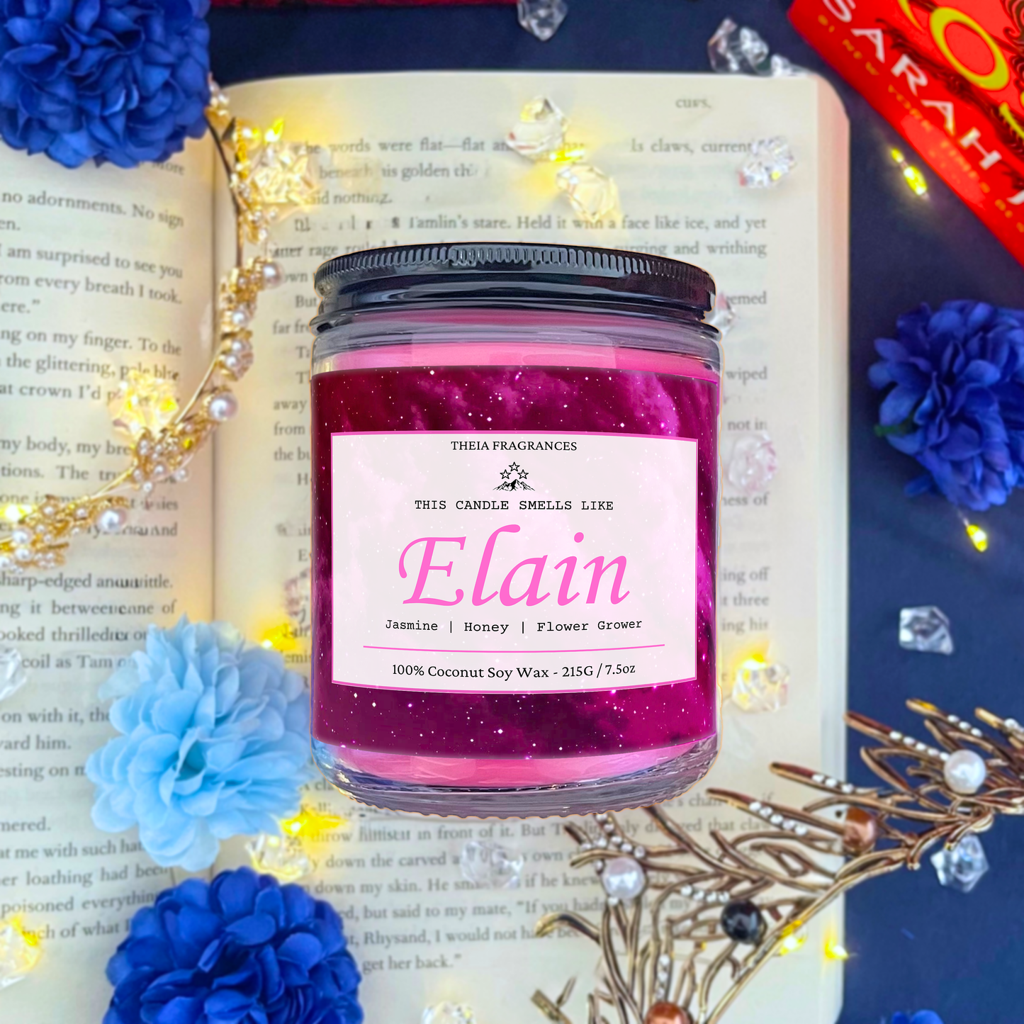 The 'Flower Grower' coconut soy wax candle by Theia Fragrances is demonstrated in the 215G glass jar with a black lid. The label features a pink galaxy. It is styled on an open book with decorative crystals and flowers.