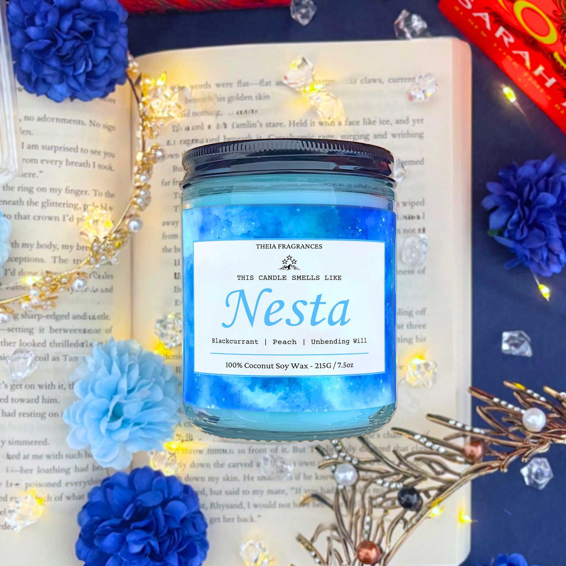 The 'Fire, Steel & Unbending Will' coconut soy wax candle by Theia Fragrances is demonstrated in the 215G glass jar with a black lid. The label features a light blue galaxy. It is styled on an open book with decorative crystals and flowers.