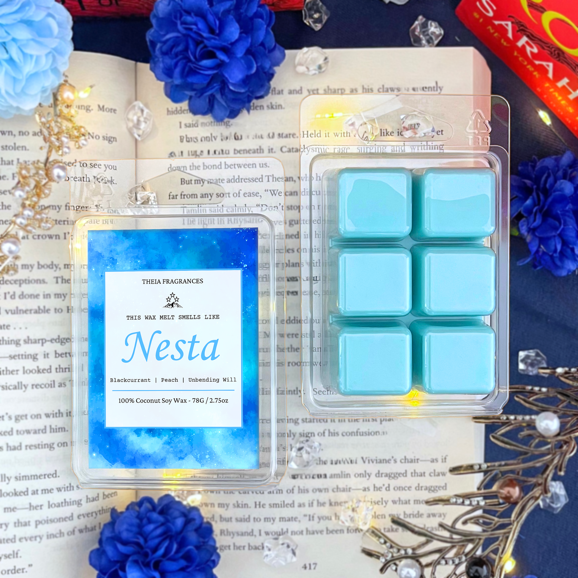 The 'Fire, Steel & Unbending Will' coconut soy wax candle by Theia Fragrances is demonstrated in the 78G rectangular wax melt. The label features a light blue galaxy. It is styled on an open book with decorative crystals and flowers.