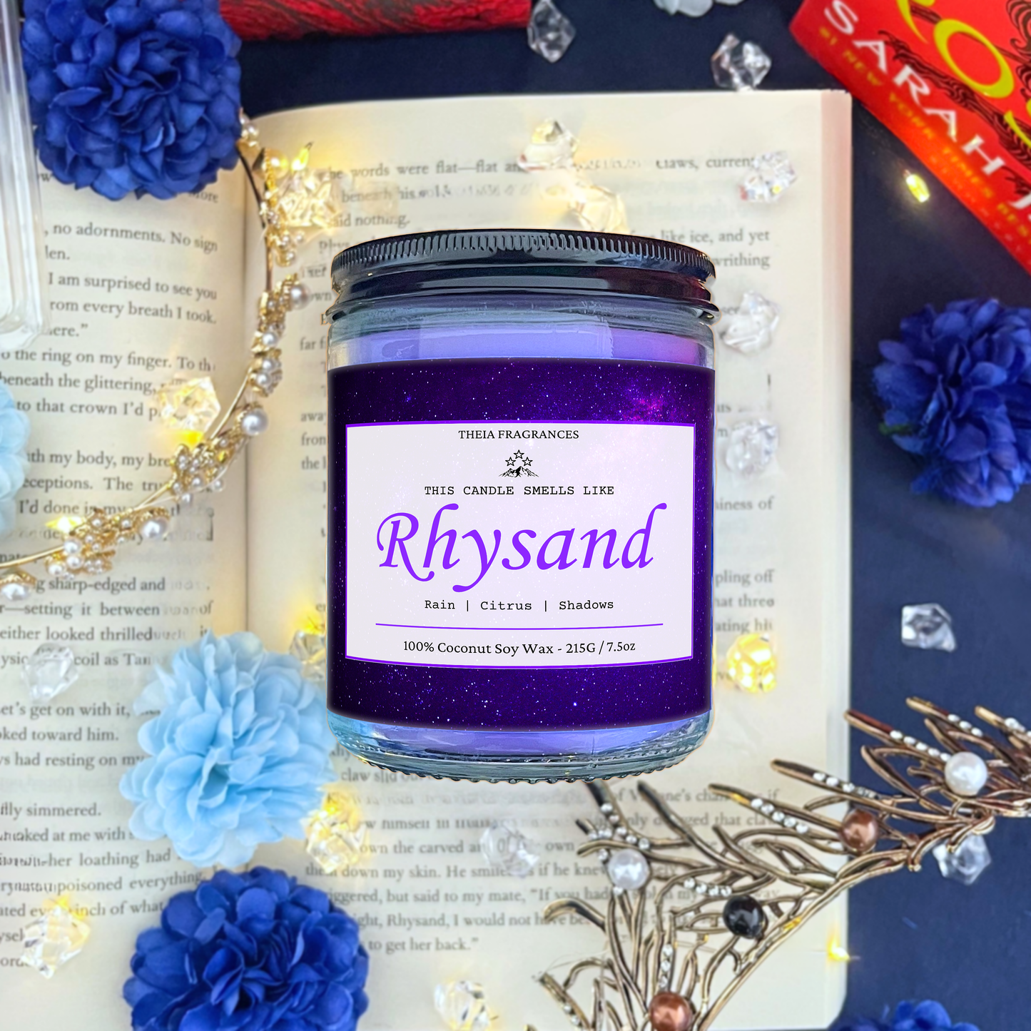 The 'High Lord of the Night Court' coconut soy wax candle by Theia Fragrances is demonstrated in the 215G glass jar with a black lid. The label features a violet galaxy. It is styled on an open book with decorative crystals and flowers.