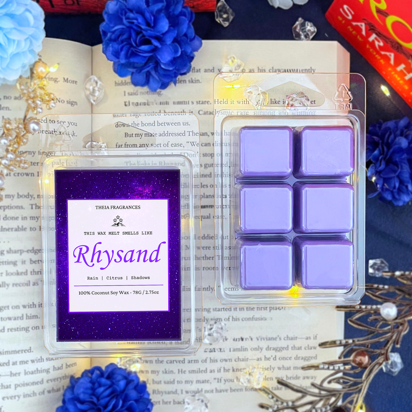 The 'High Lord of the Night Court' coconut soy wax candle by Theia Fragrances is demonstrated in the 78G rectangular wax melt. The label features a violet galaxy. It is styled on an open book with decorative crystals and flowers.