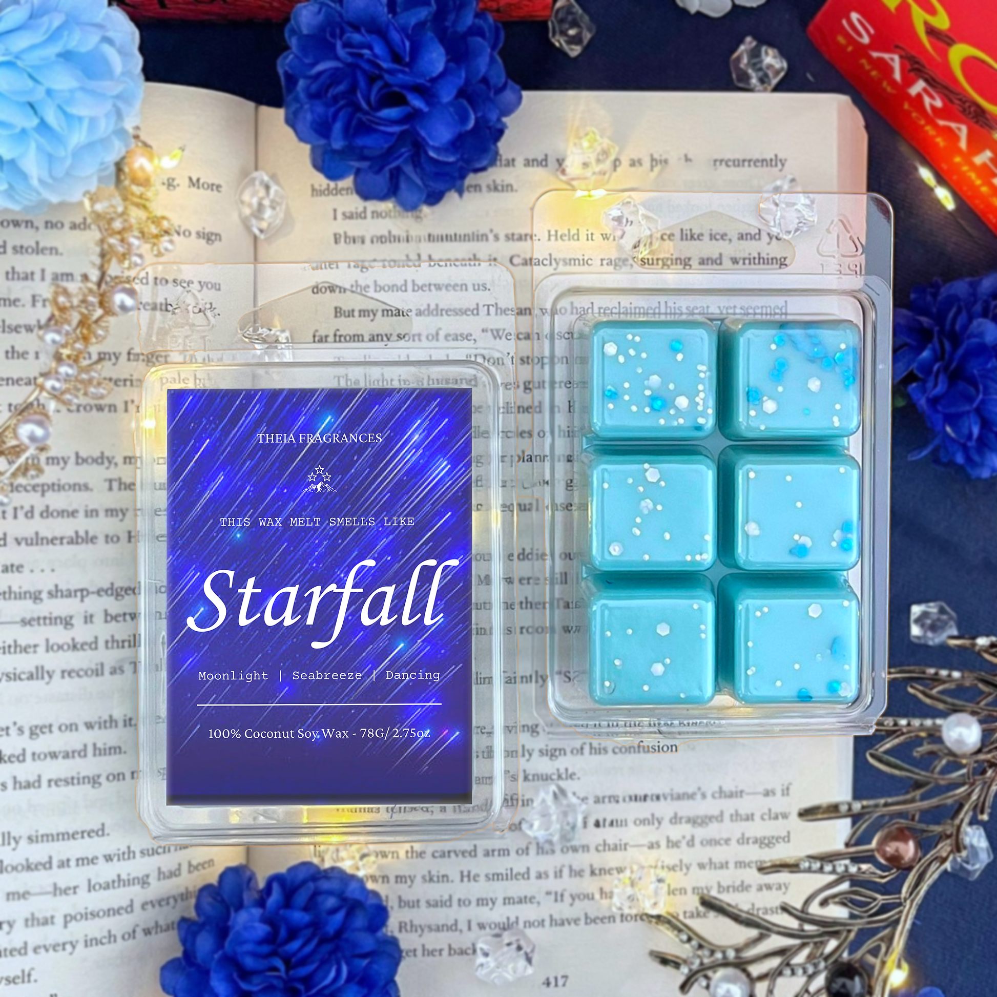 The 'Starfall' coconut soy wax candle by Theia Fragrances is demonstrated in the 78G rectangular wax melt. The label features a blue starry sky. It is styled on an open book with decorative crystals and flowers.