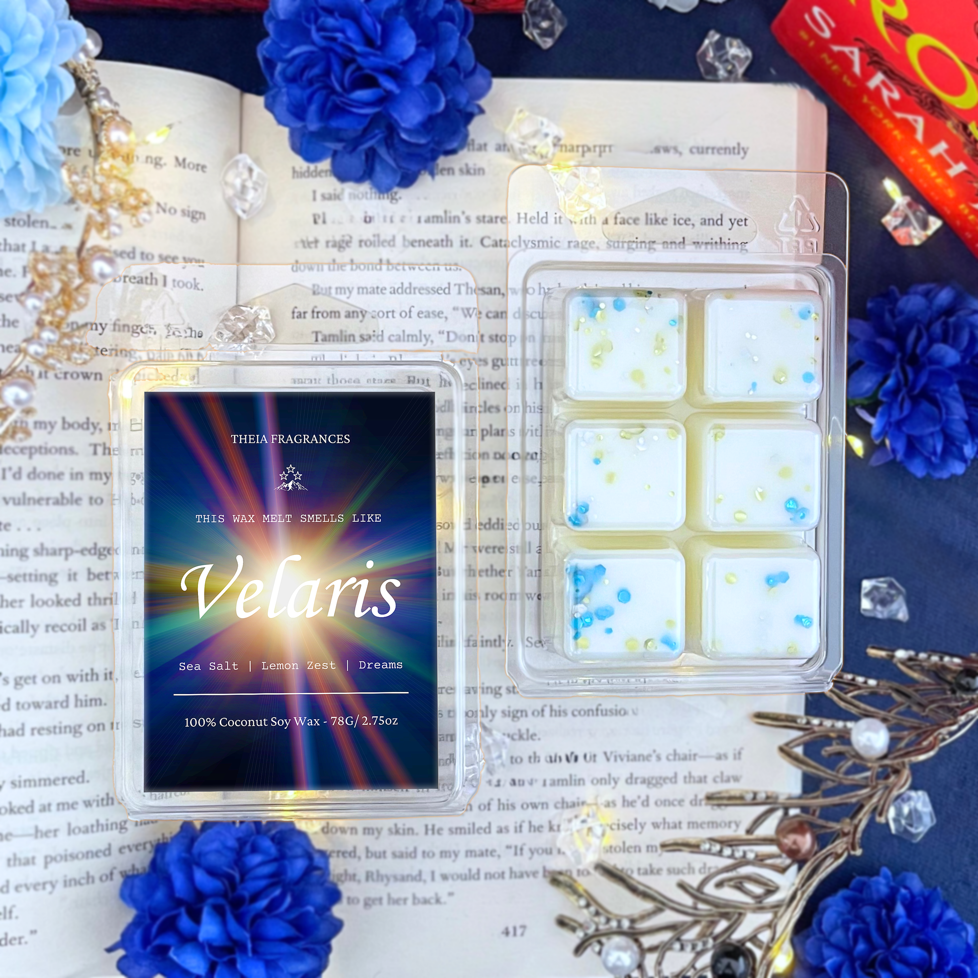The 'Velaris' coconut soy wax candle by Theia Fragrances is demonstrated in the 78G rectangular wax melt. The label features a burst of starlight. It is styled on an open book with decorative crystals and flowers.